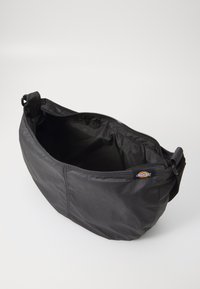 Čierna nylonová taška so zipsom, guľatým tvarom a vnútornou podšívkou. Obsahuje odolný popruh a štítok s logom na boku.