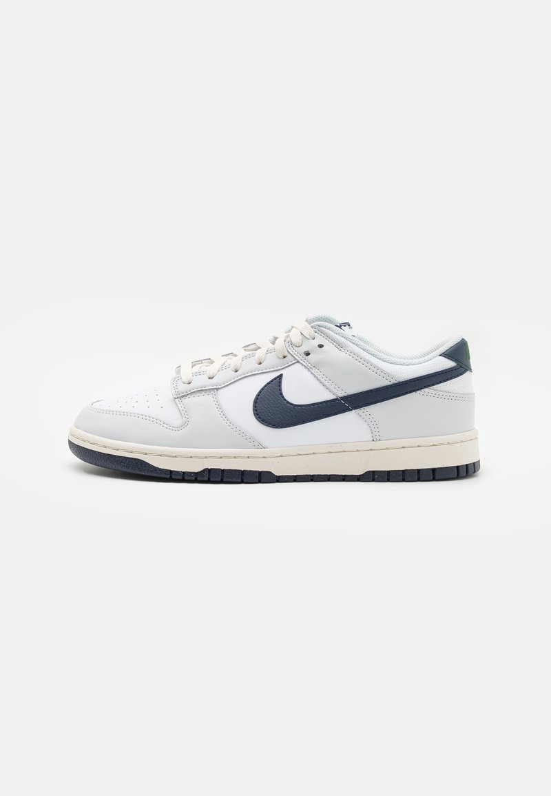 Sneaker bianco in pelle con dettagli blu navy, tomaia testurizzata, punta perforata e suola intermedia crema. Presenta lacci piatti e suola in gomma.