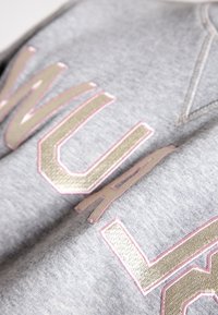 Close-up of silver and pink embroidered letters on a light gray fabric, showing texture and stitching details.