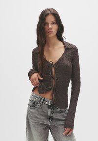 Brun, texturerad långärmad topp med krage, som har en framknutning. Matchad med högmidjade blekta grå jeans.