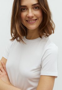 Hvid t-shirt med korte ærmer lavet af glat bomuldsstof. Har en klassisk rund halsudskæring og en tætsiddende silhuet. Ingen synlige grafikker eller mønstre.