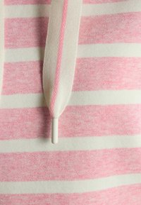 Detailný záber na pruhovanú látku v ružovej a bielej farbe s bielym a ružovým šnúrkovým uzáverom zaveseným uprostred.