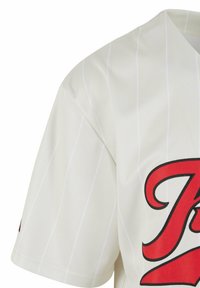 T-shirt de baseball blanc avec de fines rayures verticales, un logo brodé noir et rouge, et une texture de tissu ventilé.