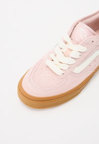 Sneaker in camoscio rosa con lacci bianchi, punta perforata e suola in gomma. Presenta una sottile striscia bianca e un'etichetta con logo stampato.