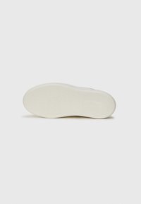 Semelle de sneaker en caoutchouc blanc avec une surface texturée, présentant des motifs circulaires et rainurés, et un logo imprimé près du talon. Couleur unie et lisse.