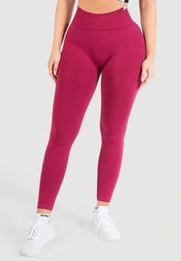 Leggings ajustados de talle alto en un color magenta profundo, hechos de tela elástica con una textura suave. Presentan un diseño elegante y cremalleras en los tobillos.