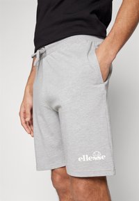 Grijze katoenen shorts met een elastische tailleband en een trekkoord, voorzien van een zijzak en een wit "ellesse" logo op het onderbeen.