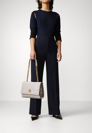 Combinaison navy avec des manches découpées, accents noirs et jambes larges ; sac à main gris clair avec un motif gaufré et une chaîne dorée.