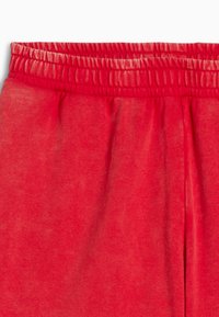 Røde sweatpants med elastisk talje og glat overflade, der har en indsamlet talje og ingen synlige lommer eller udsmykninger.