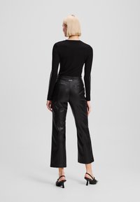 Zwarte lange mouwen top, nauw aansluitend bij de schouders, gecombineerd met hoge taille, brede zwarte leren broek, met achterzakken en minimale stiksels.