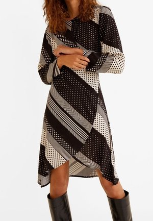 Kvinde iført en sort og hvid langærmet kjole med blandede polkaprikker og striber, kombineret med sorte knælange støvler.
