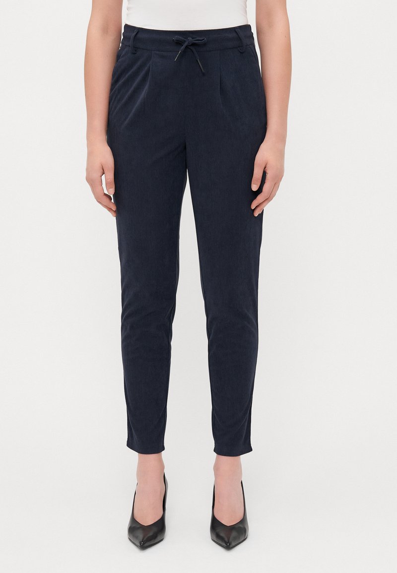 Marineblauwe corduroy broek met een getailleerd silhouet, elastische tailleband, voorplooien en een koorddetail, gecombineerd met zwarte hakken.