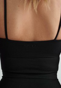 Musthave mustrakk, millel on õhukesed rihmad, sile tekstuur ja tagasi diskreetne logo detail. Kanga koostis on keha lähedalt liibuv ja veniv.