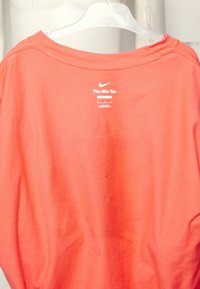 Loose-fit coral Nike tee made of soft cotton. Features a wide neckline and a small brand logo above the tag on the back.