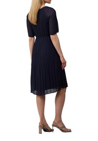 Robe plissée bleu marine à manches courtes, taille cintrée et ourlet évasé. Portée avec des sandales à talons hauts de couleur claire.