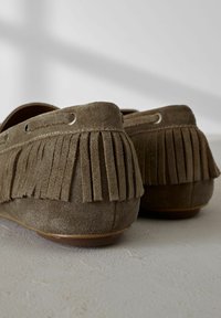 Mocasines de ante en verde oliva con acentos de flecos en el talón, suela plana y costuras decorativas a lo largo de los lados.