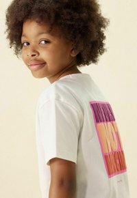 Witte katoenen t-shirt met een grafisch ontwerp op de rug in roze en oranje blokletters. Het shirt heeft korte mouwen en een ronde halslijn.