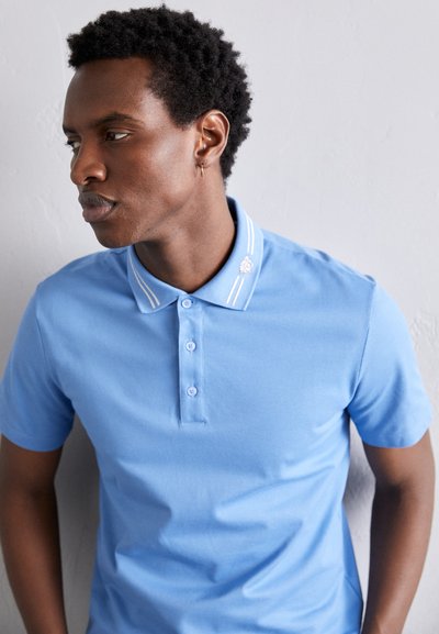 Polo de cor azul clara feito de algodão, com gola de colarinho, um pormenor de três botões e duas riscas brancas na gola.