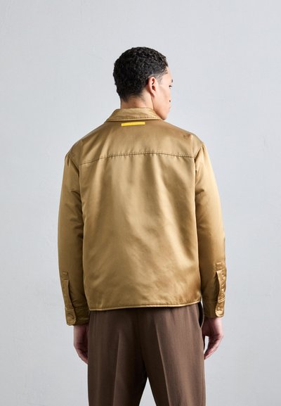 Brown satin jacket with a simple collar, featuring a yellow accent at the back. Buttons on cuffs, smooth texture, and relaxed fit.