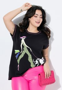 Camiseta negra con un gráfico colorido de una figura estilosa paseando un perro. Presenta mangas cortas, ribete rosa y un corte holgado. Combinada con leggings rosas y un bolso acolchado rosa.