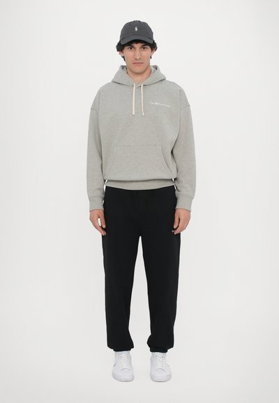 Hanorac gri cu glugă, dotat cu o buzunar frontal și șnururi crem, asortat cu pantaloni de trening negri. Adidașii albi completează ținuta.