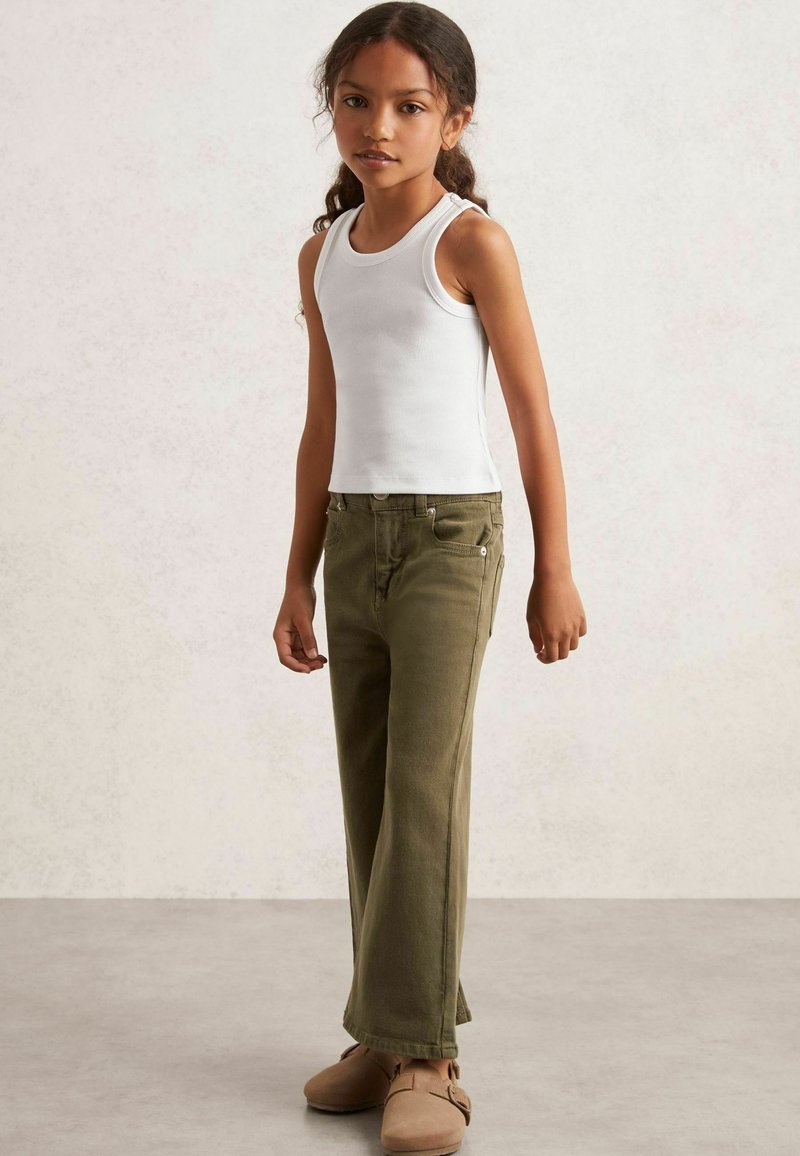 Weißes Tanktop, olivgrüne Hose und weiche beigefarbene Schuhe. Das Outfit hat ein schlichtes Design ohne sichtbare Muster oder Hardware-Details.