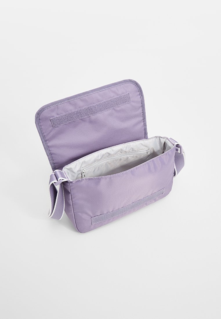 Bolso de hombro de tela morada con cierre de solapa, que presenta un interior gris y una correa ajustable. Un bolsillo en el interior, textura suave.
