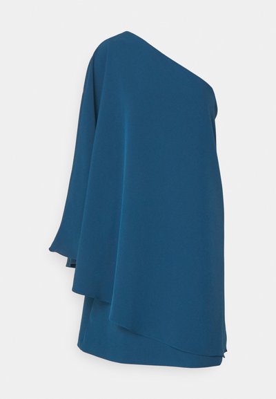 Top με έναν ώμο σε σκούρο τιρκουάζ ύφασμα, με ρέουσα σχεδίαση, ασύμμετρο διπλωτό και μαλακή υφή. Χωρίς ορατούς κλειδώματα.