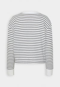 Maglione bianco a coste con righe orizzontali blu navy, dotato di maniche lunghe e scollatura arrotondata. I polsini sono di un bianco uniforme.