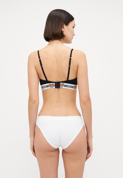 Crna braletica s podesivim remenima i Moschino logom; uparen s bijelim kupaćim gaćicama. Glatka tkanina, minimalistički dizajn, bez uzoraka.