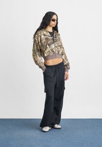 Besluttet camouflage hoodie med en frontlynlås og grå manchetter, parret med løse sorte cargo-bukser med sidelommer og snor.