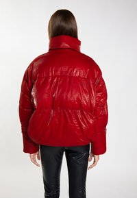 Giacca puffer rossa con finitura lucida, colletto alto e polsini elasticizzati. Progettata per il calore; presenta una silhouette ampia e sezioni imbottite.