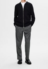 Svart zip-up stickad tröja, grå rutiga byxor och svarta skor. Har en krage och ett texturerat tyg för toppen.