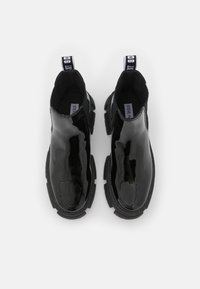 Bottines en cuir verni noir avec une semelle épaisse, des panneaux latéraux élastiques et des tirants. Présentent une texture lisse et une forme de bout arrondi.