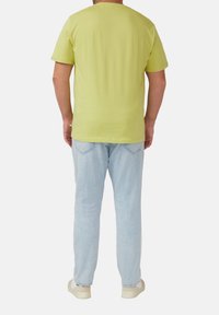 T-shirt à manches courtes, vert lime vif avec un col rond, associé à un jean bleu clair et des baskets de couleur clair. Design minimal sans motifs.