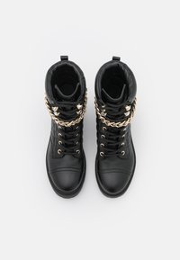 Botas de cuero negro hasta el tobillo con un cuello acolchado, acentos de cadena dorada y costuras en contraste. Presentan un diseño de caña alta y puntera redonda.