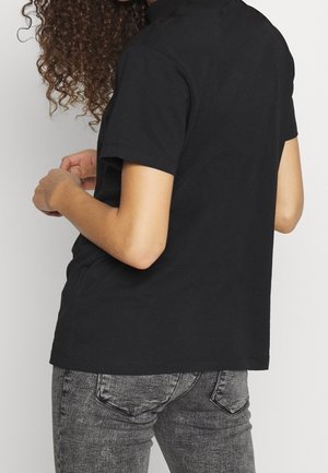 Camiseta de algodón negra con mangas cortas, corte relajado, diseño sencillo sin gráficos visibles, combinada con jeans grises con textura desgastada.