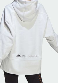 Vit hoodie med en avslappnad passform, huva och ribbade ärmslut. Har svart Adidas och Stella McCartney-logotyp på nedre delen av ryggen.