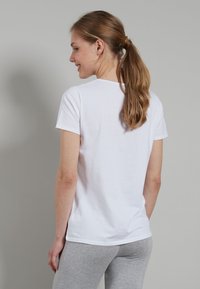 White cotton t-shirt with short sleeves and a round neckline, featuring a smooth texture and relaxed fit, shown from the back.