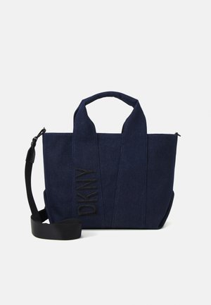 Tmavě modrá džínová taška s dvěma krátkými uchy, nastavitelným černým ramenním popruhem a svislým logem „DKNY“ na přední straně.