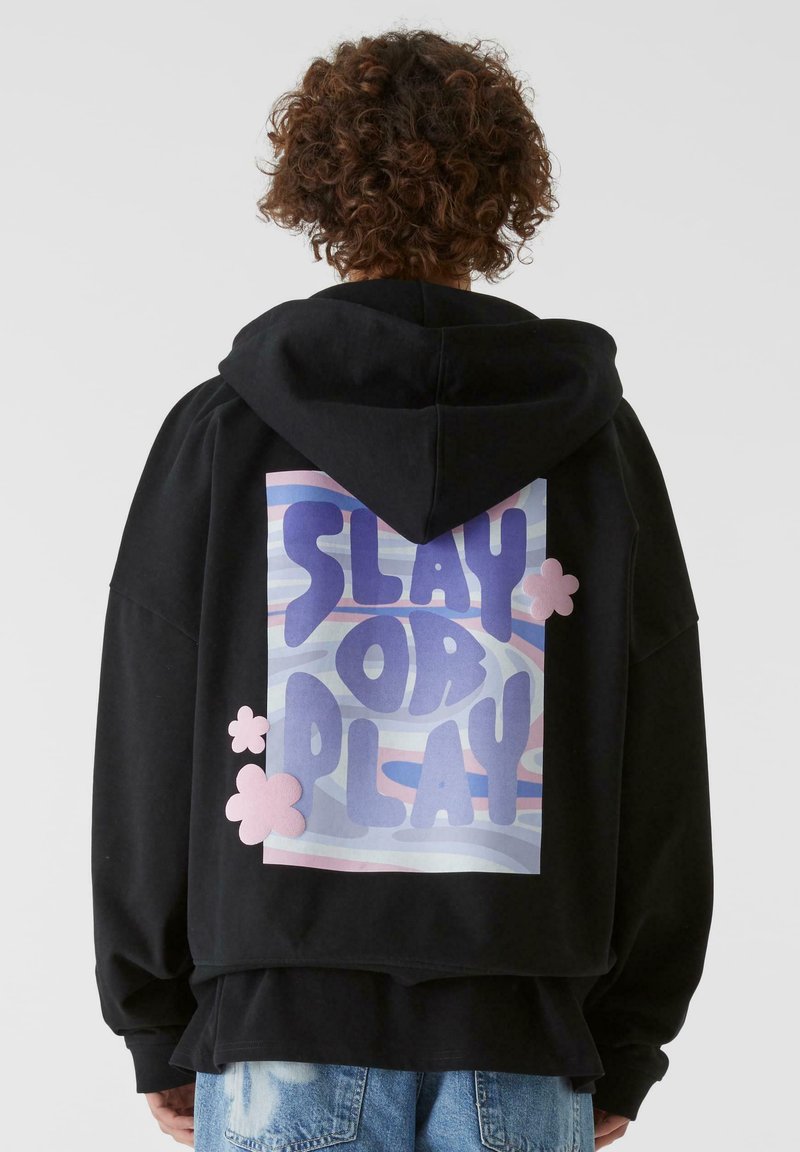 Svart hettegenser med et stort ryggramme som leser "SLAY OR PLAY" i lilla og rosa, med sky-lignende mønstre og rosa detaljer.