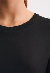 Suéter negro de punto que presenta un cuello acanalado, textura suave y un diseño ajustado, vista en ángulo que se centra en el cuello y la parte superior de la tela.