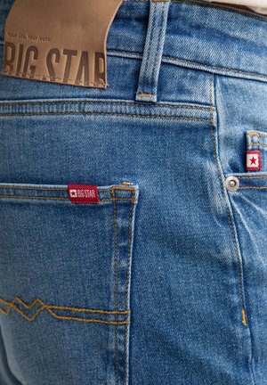 Jasnoniebieskie dżinsy z denimu z skórzaną naszywką z napisem "BIG STAR" oraz czerwoną metką marki na tylnych kieszeniach z białymi akcentami w kształcie gwiazd.