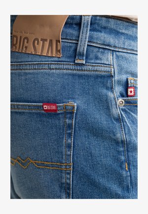 Jasnoniebieskie dżinsy z denimu z skórzaną naszywką z napisem "BIG STAR" oraz czerwoną metką marki na tylnych kieszeniach z białymi akcentami w kształcie gwiazd.