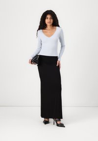 Light blue long-sleeve top with a scalloped neckline, paired with a black, form-fitting maxi skirt and black heeled shoes. Small black handbag held.
