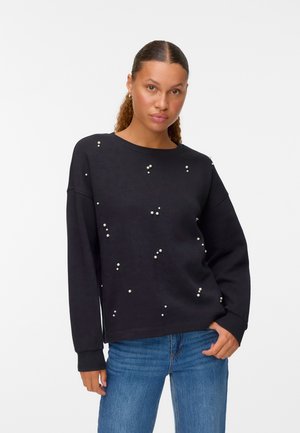 Svart sweatshirt med lös passform, dekorerad med spridda pärl detaljer. Långa ärmar och rund halsringning, ihop med blå jeans.