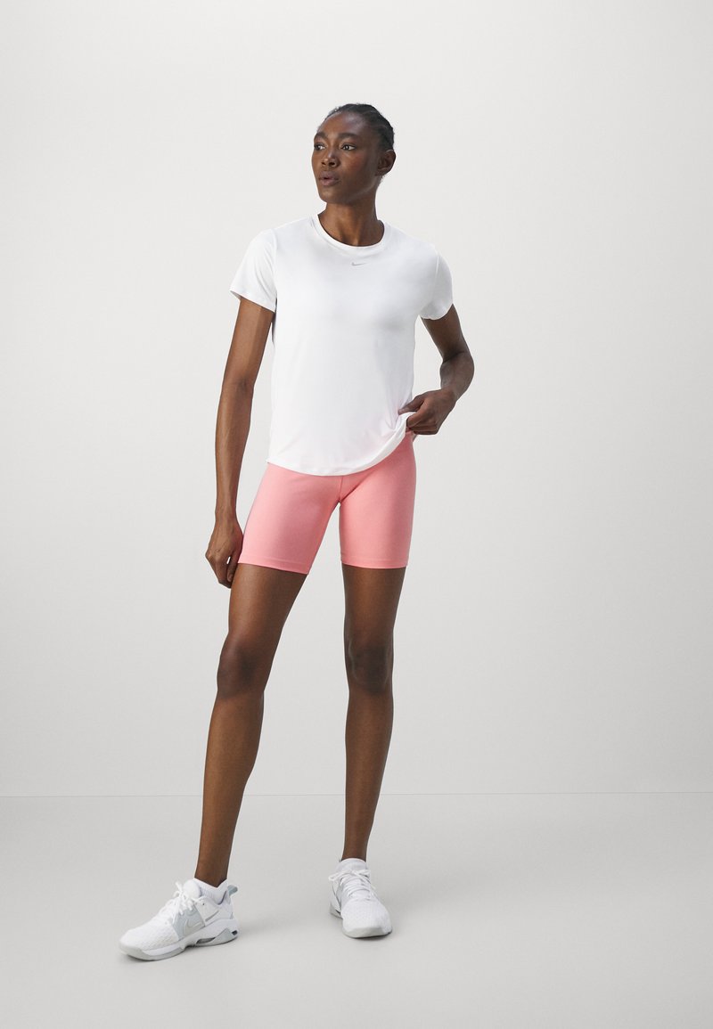 Sportliches Outfit mit einem weißen Kurzarmshirt und rosa Shorts. Die Person trägt weiße Sneakers mit grauen Akzenten.