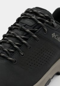 Schwarze Columbia-Schuhe mit strukturiertem Obermaterial, durchbrochener Gestaltung und kontrastierenden Schnürmustern. Mit schwarzen Schnürsenkeln und einer hellgrauen Sohle.