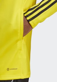 Gelbes Sportshirt aus atmungsaktivem Material, mit einem strukturierten Mesh-Einsatz, drei schwarzen Streifen an den Ärmeln und einem "AEROREADY" Logo.