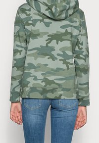 Groen camouflage capuchontrui met lange mouwen, zachte stof en geribbelde boorden. Het heeft een casual pasvorm en een licht afgeronde zoom aan de achterkant.